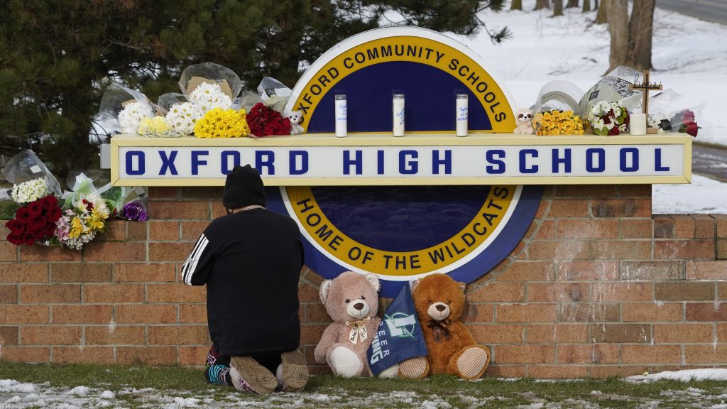 A well wisher kneels to pray at a memorial on the sign of Oxford High School in Oxford, Mich., Wednesday, Dec. 1, 2021.