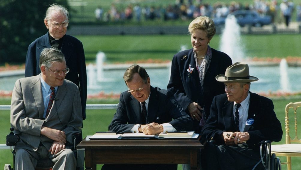 President George H. W. Bush signs the Americans with Disabilities Act surrounded by men in wheelchairs in 1990
