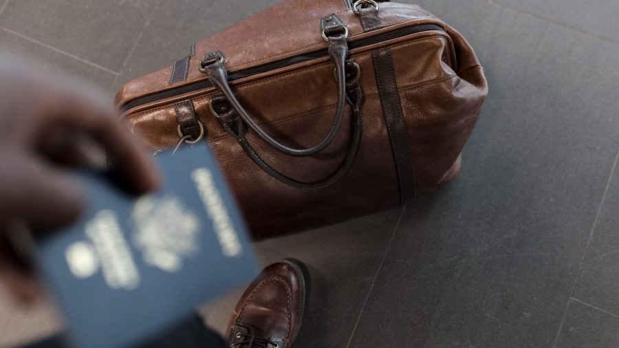 Stock photo of a person holding their passport while their luggage bag is at their feet.
