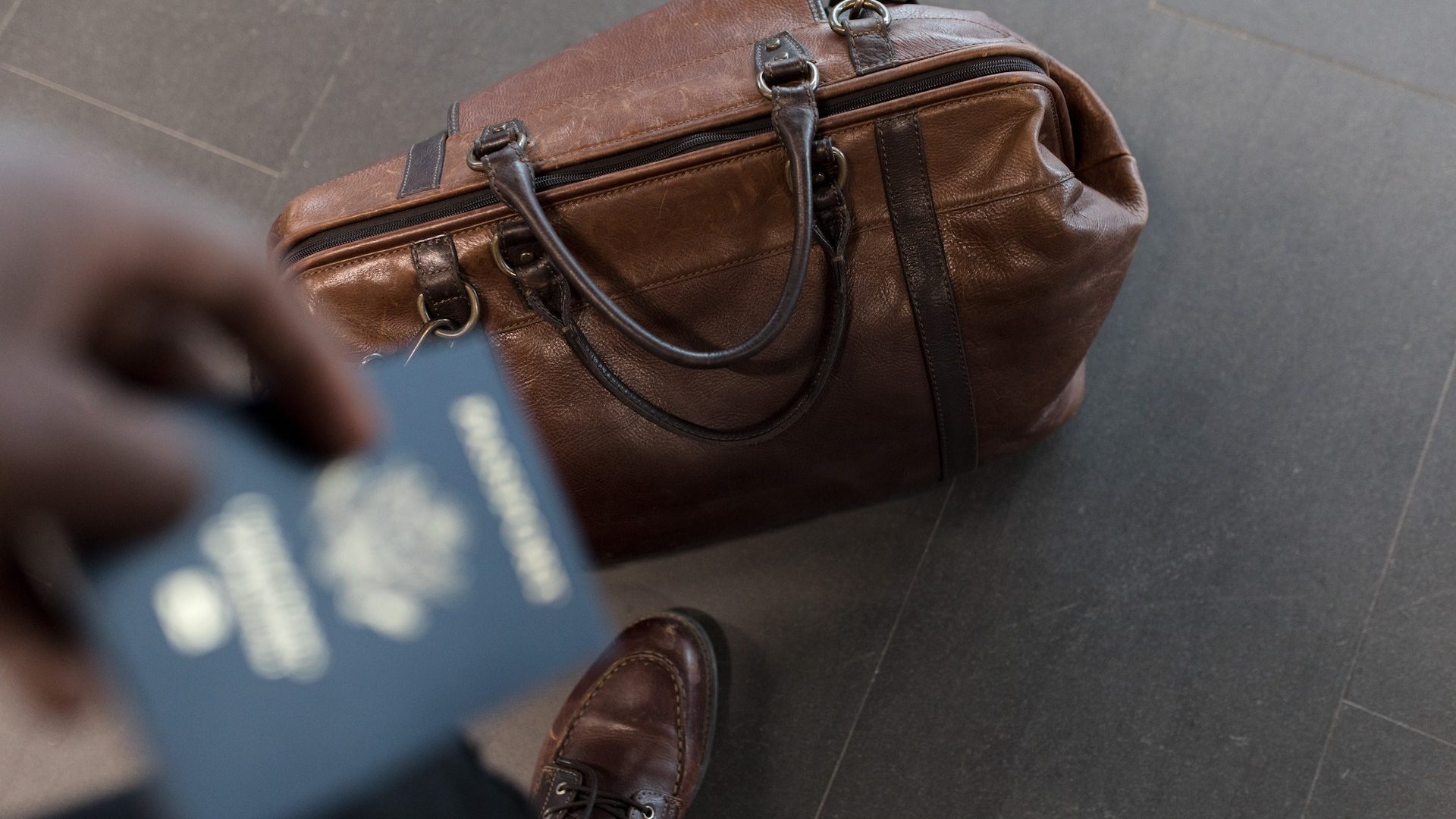 Stock photo of a person holding their passport while their luggage bag is at their feet.