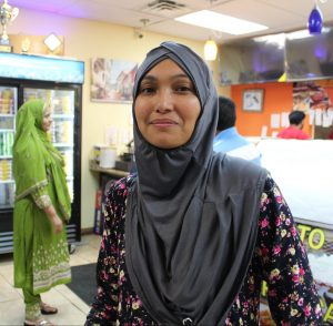 A woman named Tammana Khanom stands in a grey hijab and dark floral dress inside the take out area at Bismillah Kabob N Curry in Warren.