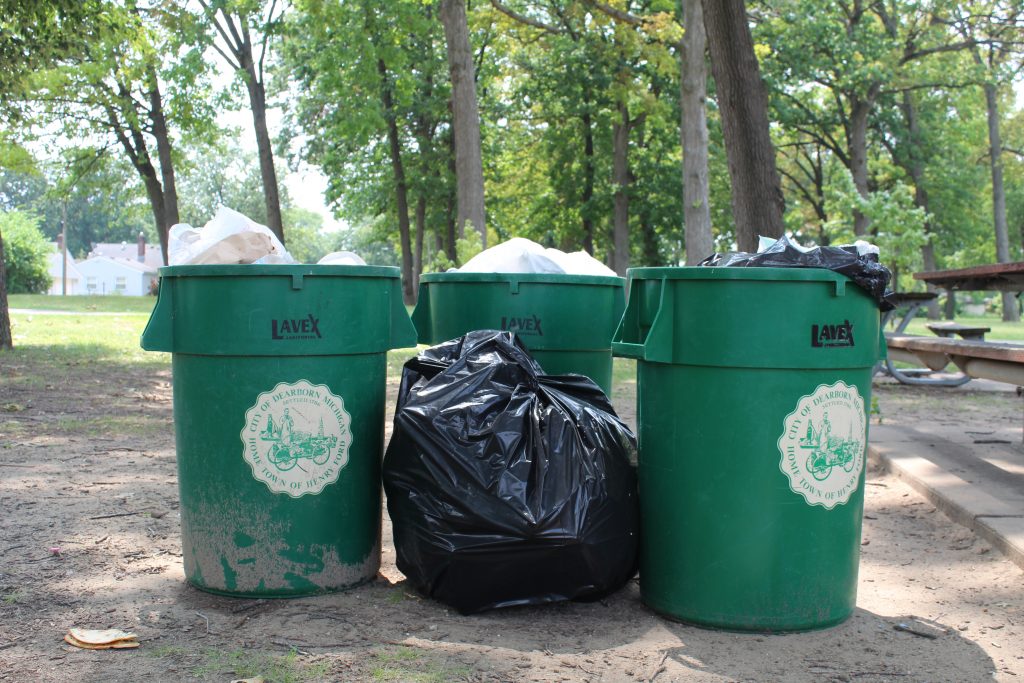 Three trash cans and a trash bag sit in a Dearborn park.