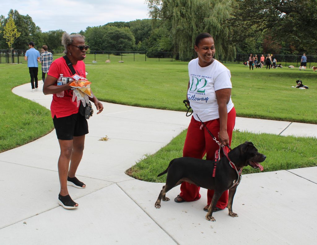 Two women stand with a pitbull terrier on a leash inside the park.