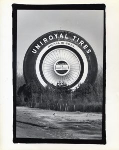 Black and white image of a massive tire-shaped building on the side of the road