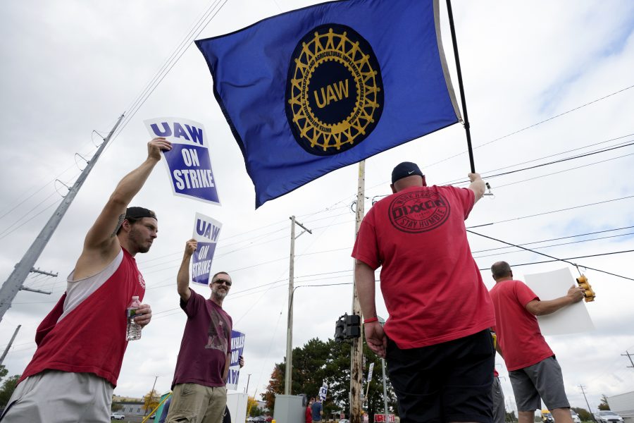 United Auto Workers members hold picket signs and a flag near a General Motors Assembly Plant in Delta Township, Mich., Friday, Sept. 29, 2023.