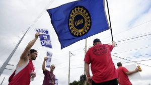 United Auto Workers members hold picket signs and a flag near a General Motors Assembly Plant in Delta Township, Mich., Friday, Sept. 29, 2023.