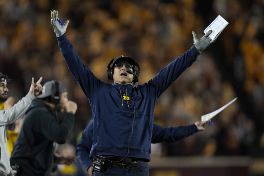 FILE - Michigan head coach Jim Harbaugh signals for a touchdown while looking at the replay board during the first half of an NCAA college football game against Minnesota, Saturday, Oct. 7, 2023, in Minneapolis. When Jim Harbaugh and the University of Michigan have their day in court, trying to at least pause punishment from the Big Ten for a sign-stealing scheme, sports law experts will be among those watching how the extraordinary confrontation plays out.