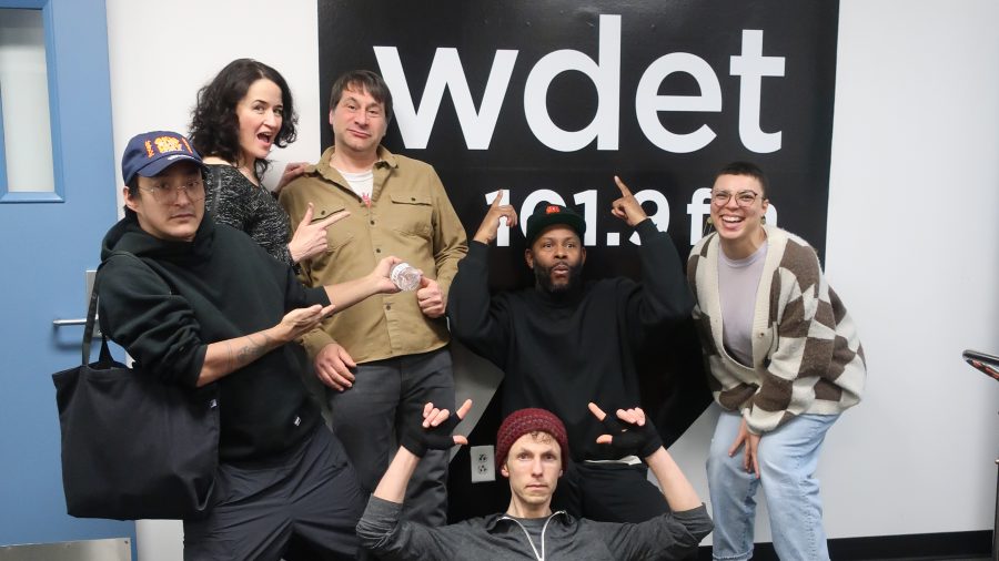 New WDET music hosts pose in front of the WDET logo.