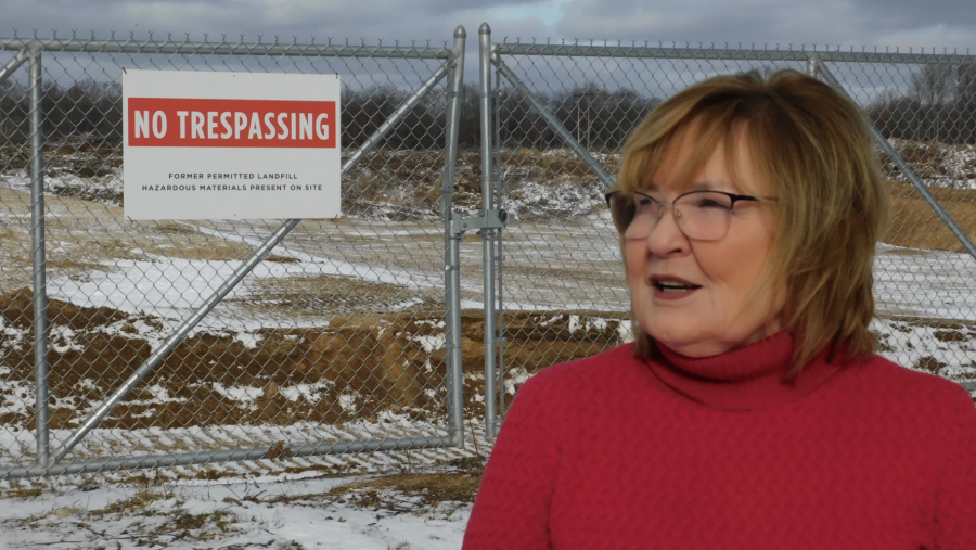 Sandy Wynn-Stelt stands next to the entrance to a PFAS dump site across from her home in Belmont, Mich.