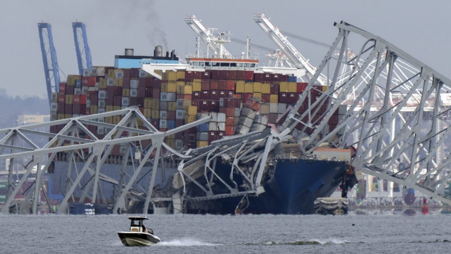 A boat moves past a container ship as it rests against wreckage of the Francis Scott Key Bridge on Tuesday, March 26, 2024, as seen from Pasadena, Md.