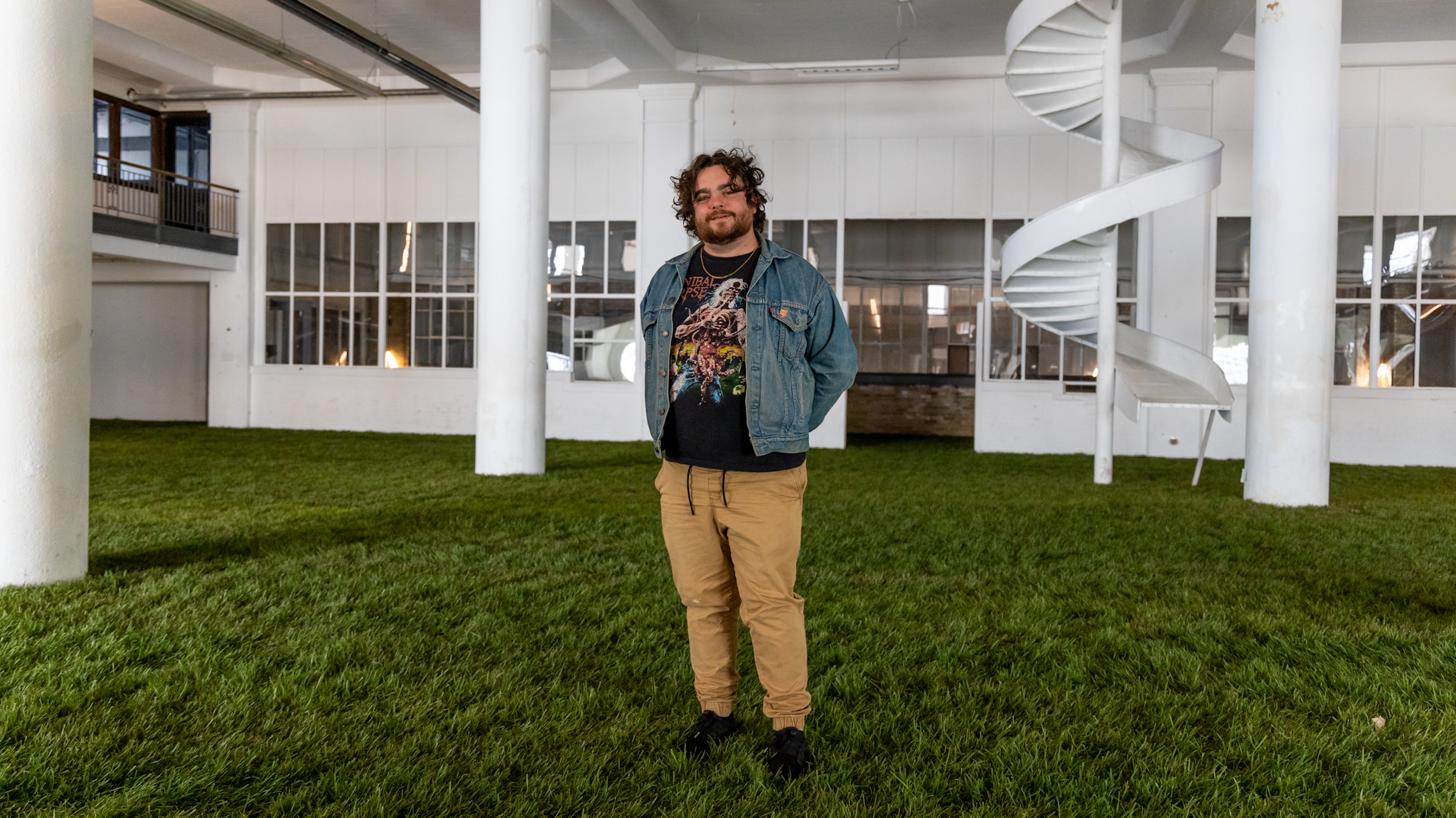 Ryan Patrick Hooper poses on the grass set inside the Boyer Campbell Building in Detroit for the Petrichor botanical art installation on May 30, 2024. (Photo credit: Tayler Simpson, WDET)