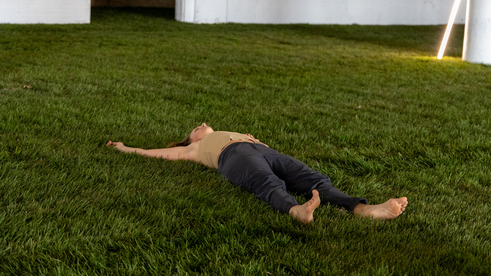 Woman lays down on the grass set inside the Petrichor display.