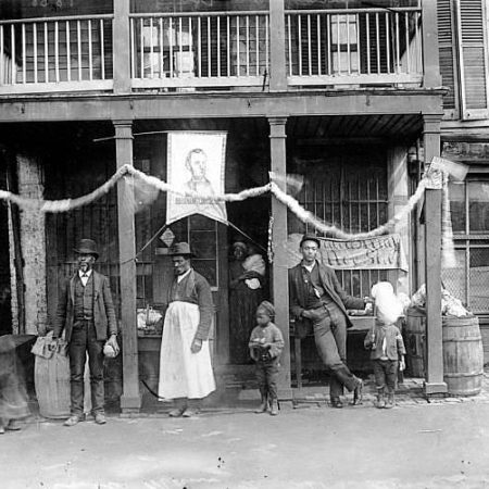 A group poses in front of a shop at E. Main Street near 21st Street in Richmond, Va., on Juneteenth, circa 1900.