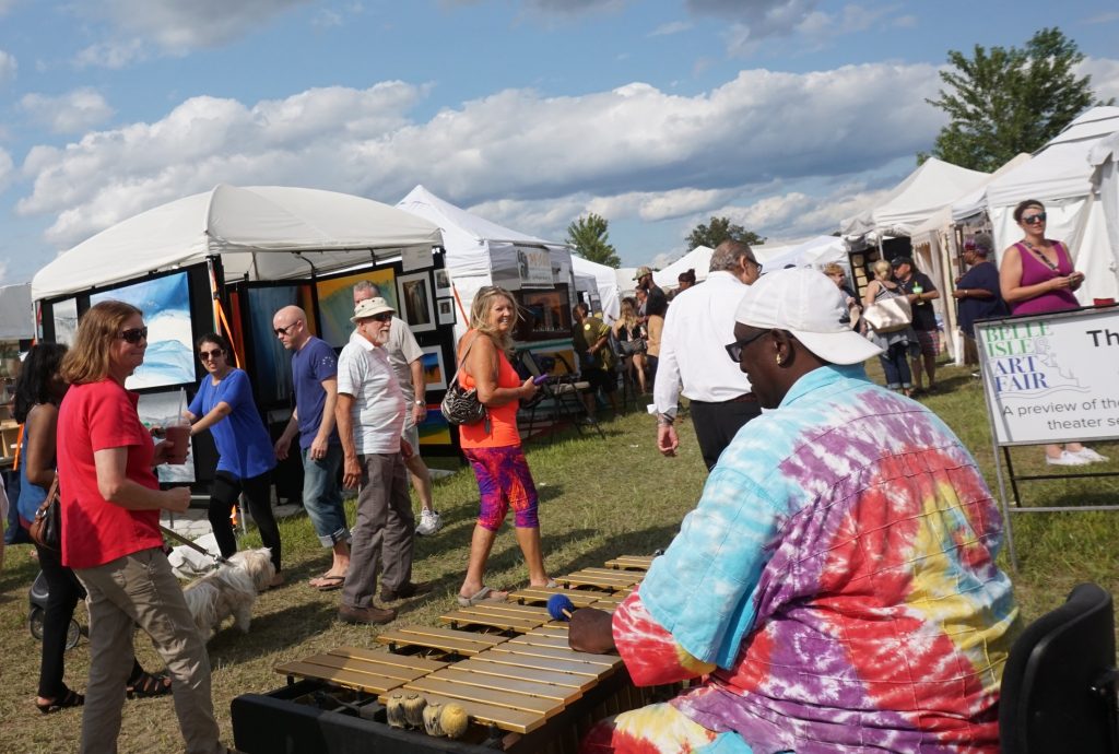 Guests peruse the Belle Isle Art Fair as a musician plays a xylophone.