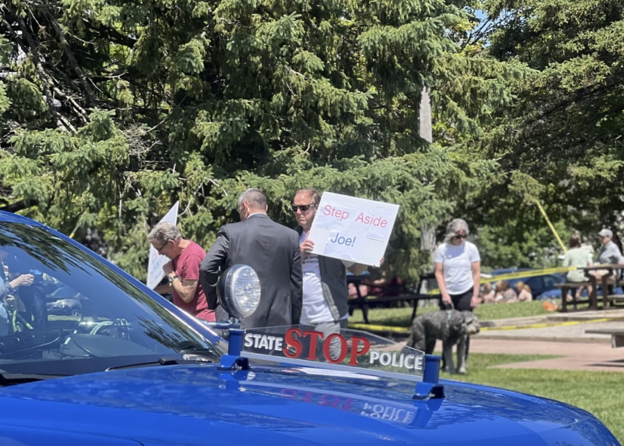 A man carrying a sign that reads "Step Aside Joe" interacts with a secret service officer outside a new Biden-Harris campaign office in Traverse City.