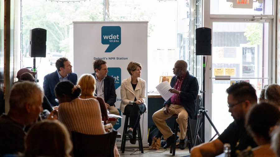 WDET News Director Jerome Vaughn engages with panelists in front of a WDET banner during Smart Politics II on July 10, 2024 at The Rind in Berkley. Audience members look onward.