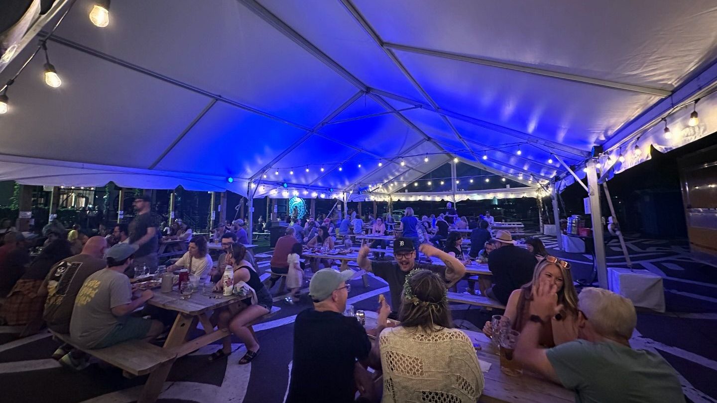 People sit at picnic tables under an outdoor tent