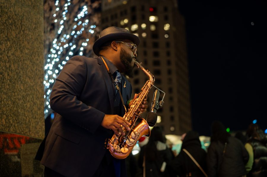 A saxophonist performs illuminated by string lights