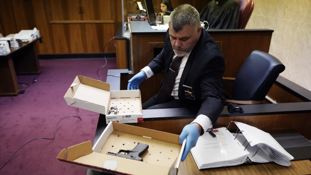 Oakland County Sheriff Lt. Tim Willis reaches for the gun Ethan Crumbley used to kill four students and injured six others and a teacher in November 2021 at Oxford High School, in court, Thursday, July 27, 2023, in Pontiac, Mich. Oakland County judge Kwame Rowe is hearing evidence starting Thursday to help him decide whether the teen who killed four students and injured six others at Oxford High School should be sentenced to prison without the chance of parole.