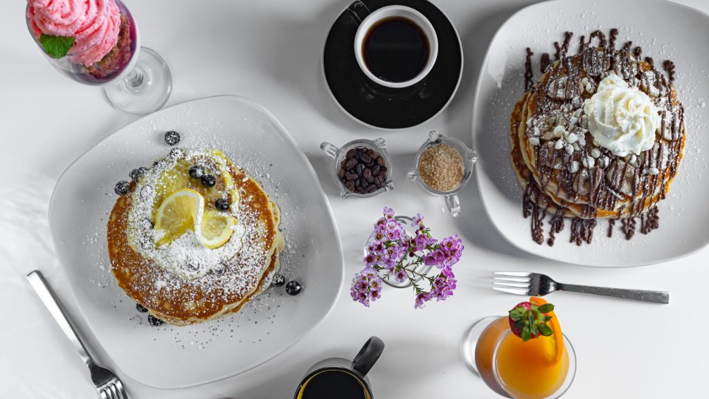 A table with intricately decorated pancakes, coffee and juices