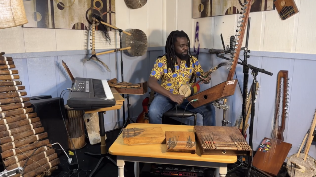A man sits surrounded by wood and electric musical instruments