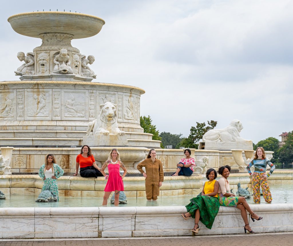 8 women pose standing in and on the James Scott Memorial Fountain in Detroit