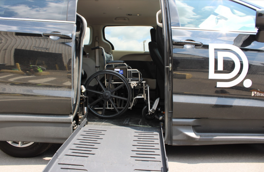 A mini van is parked with its side door open. A ramp is coming out the side and you can see a wheelchair in the van.