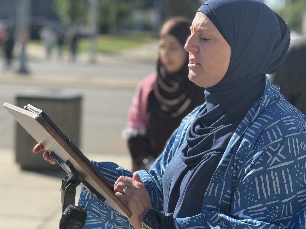 A woman wearing blue speaks at an improvised podium outside.