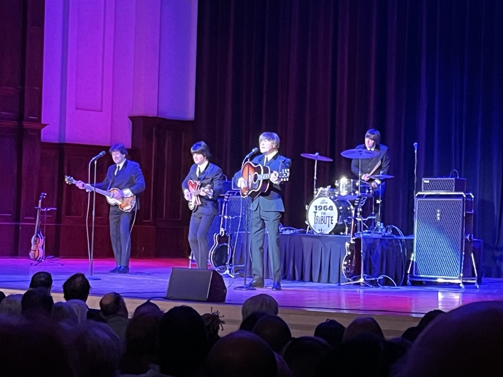 The Beatle cover band is washed in purple-blue stage lights as they perform playing their instruments live.