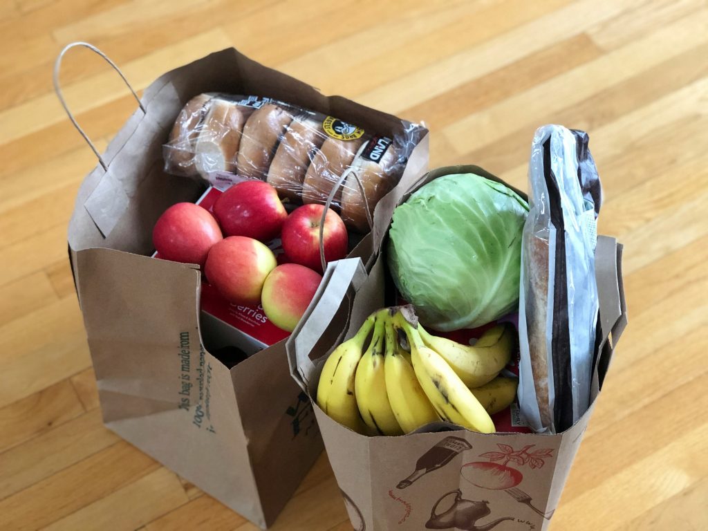 Two small bags of produce from a grocery store. They include apples, bananas, and lettuce.