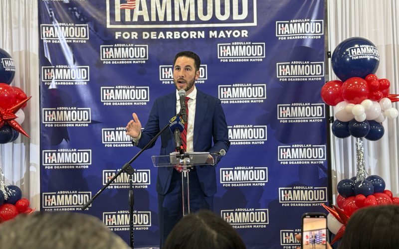 Hammoud stands in front of a backdrop of his campaign logo, speaking to the crowd gathered to watch the votes for Dearborn mayor come in.