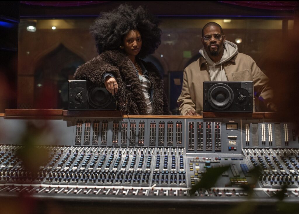 Vocalist Liv.e stands next to drummer and producer Karriem Riggins in a production booth.