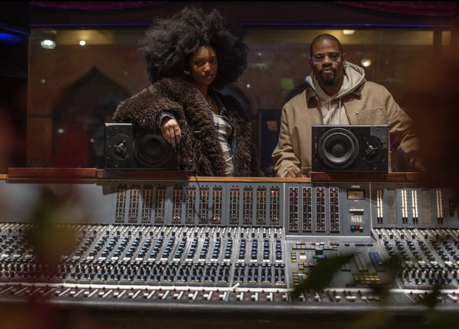 Vocalist Liv.e stands next to drummer and producer Karriem Riggins in a production booth.