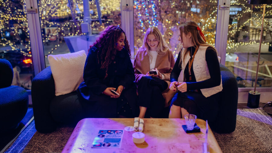 Three girls play trivia on a couch with Christmas lights in the background